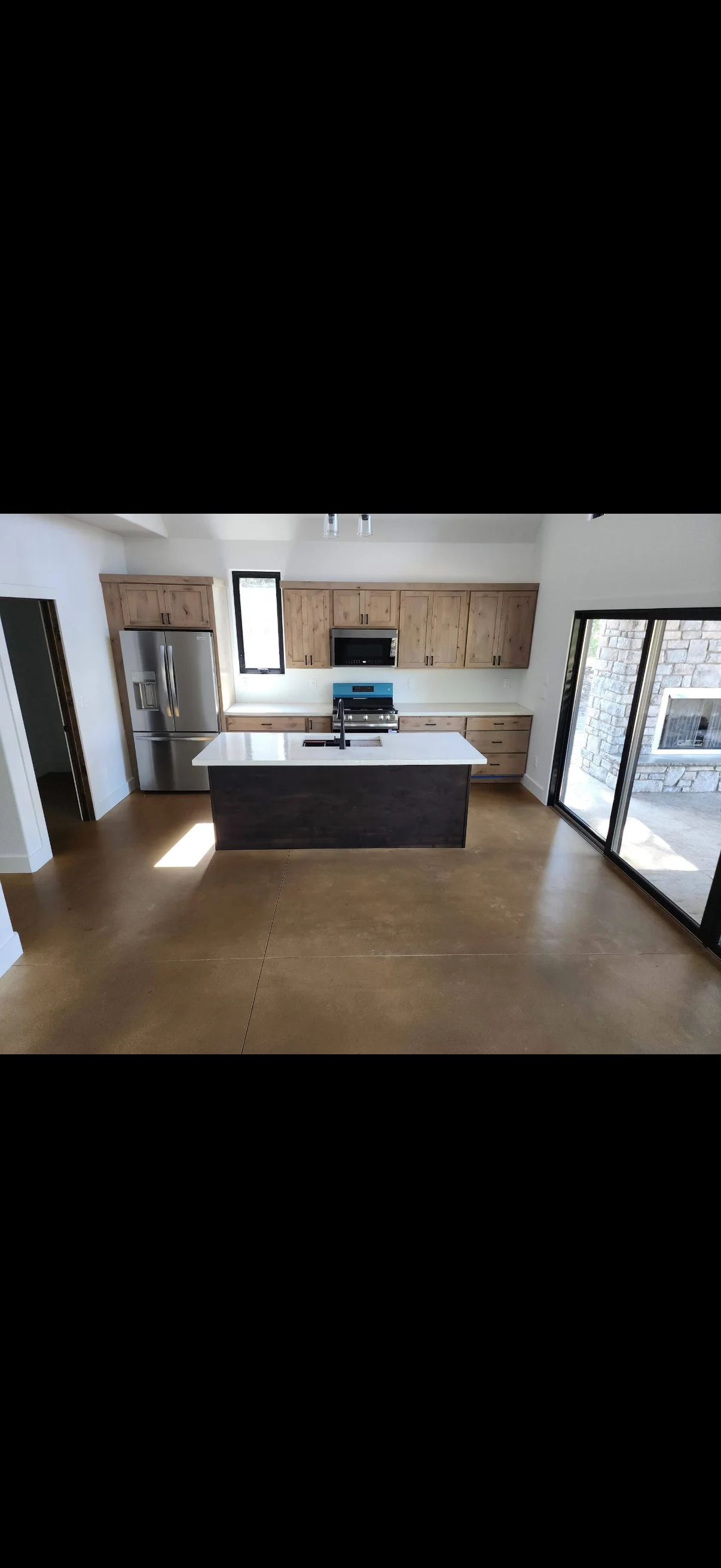 Kitchen with wood cabinets, black island, white countertop, stainless appliances, and polished concrete floors