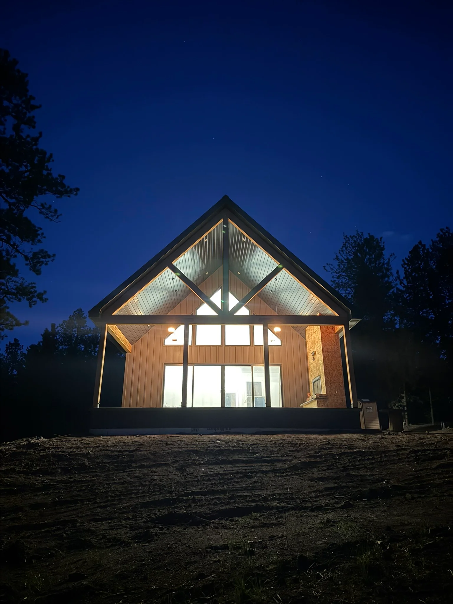 Modern gable home with steel frame, wood siding, and large windows illuminated at dusk