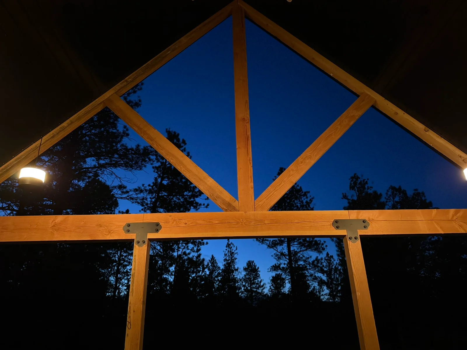 Timber frame pavilion with peaked roof, exposed wooden beams, and large gable windows at dusk