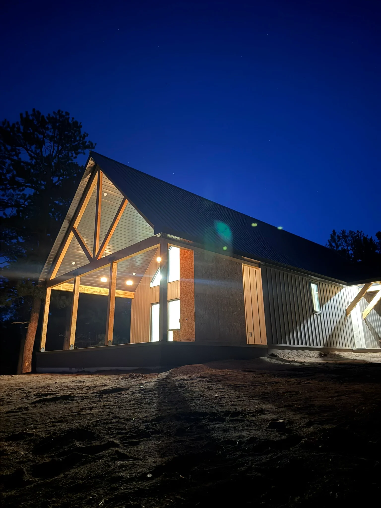 Modern home with wood siding, metal roof, brick chimney, and large windows at dusk