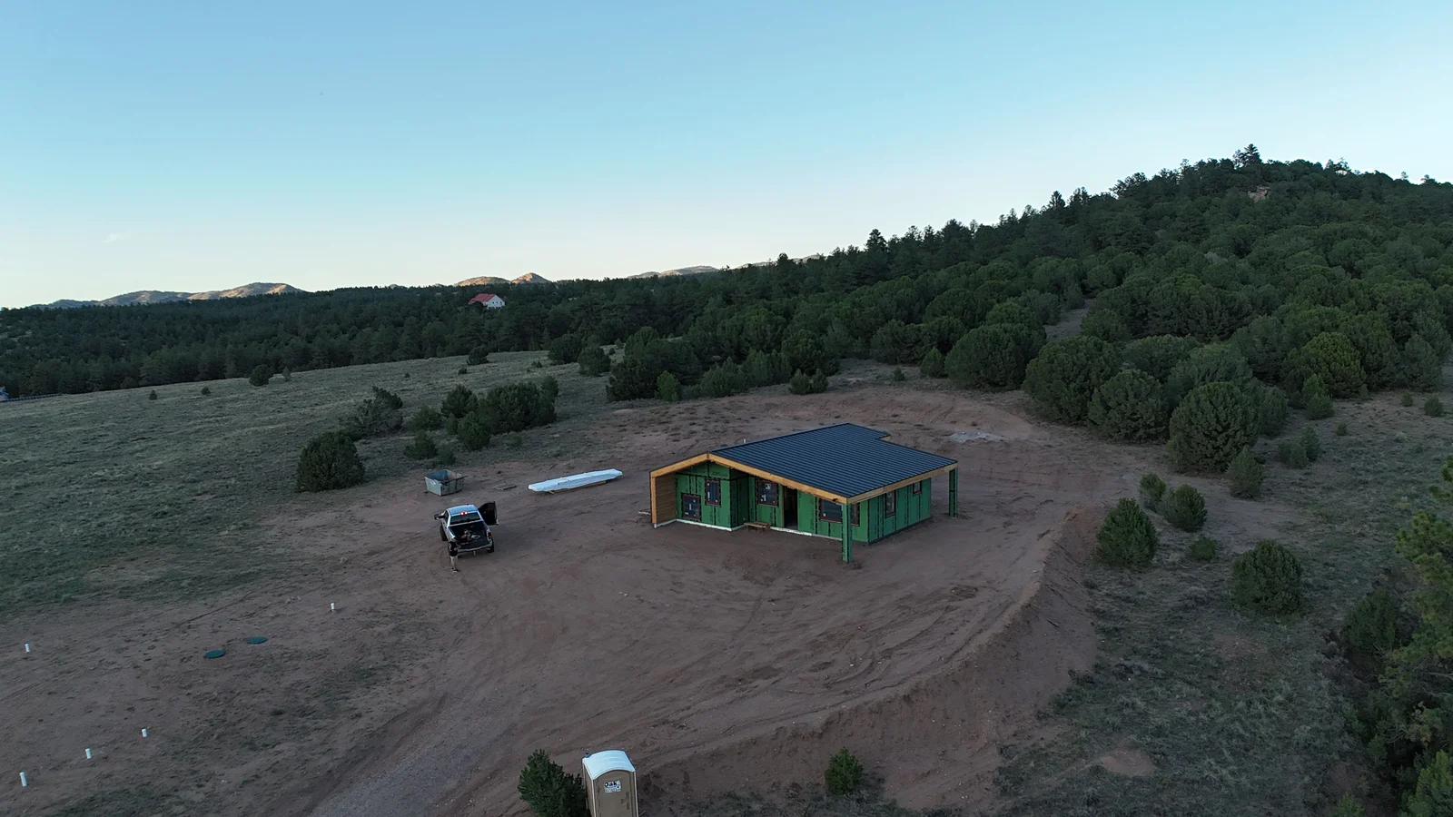 A completed off-grid custom home on a rural Custer County, Colorado parcel, with solar panels on the roof and mountain terrain visible in the background. The structure shows a steep-pitched roof designed for snow load at high elevation.